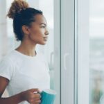 Kvinne med kaffekopp ser ut av vinduet i rolig stund