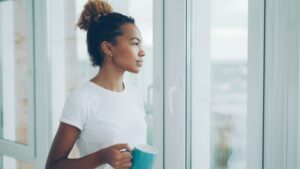 Kvinne med kaffekopp ser ut av vinduet i rolig stund