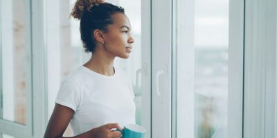 Kvinne med kaffekopp ser ut av vinduet i rolig stund